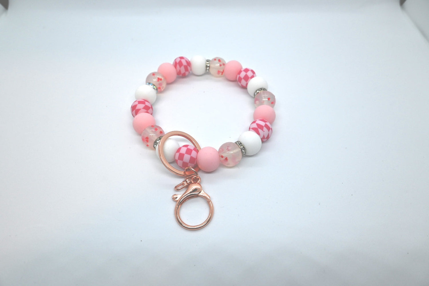 a keychain wristlet that has pin, pink checkered, white, and heart confetti beads as well as silver rhinestone spacers